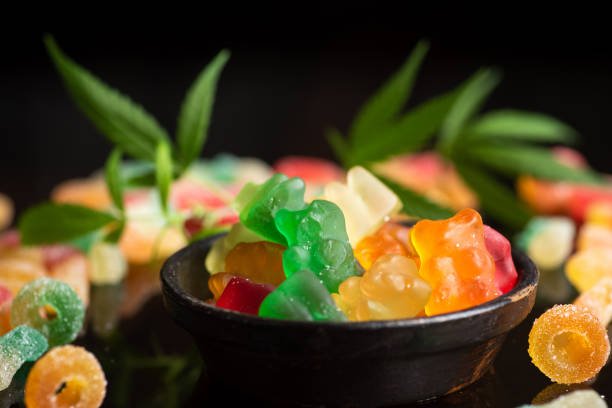 Close-up of colorful delta 9 THC gummies in a jar being held by a person, highlighting cannabis edibles and lifestyle consumption